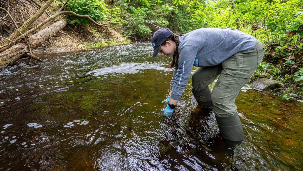 Researcher in boots collects water sample from river