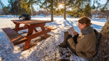 A student reads at the base of a tree in this winter scene