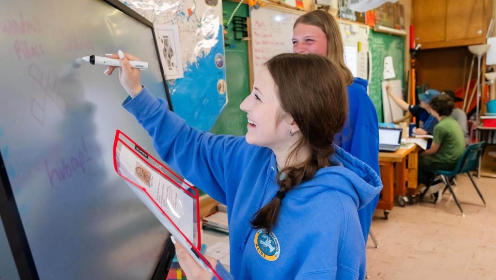 A photo of two students writing on an interactive monitor