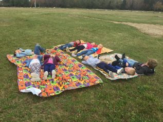 Young children lying on blankets in the green grass, looking up at the sky