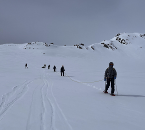 Line of students with a rope connecting them crossing glacial snowfield.