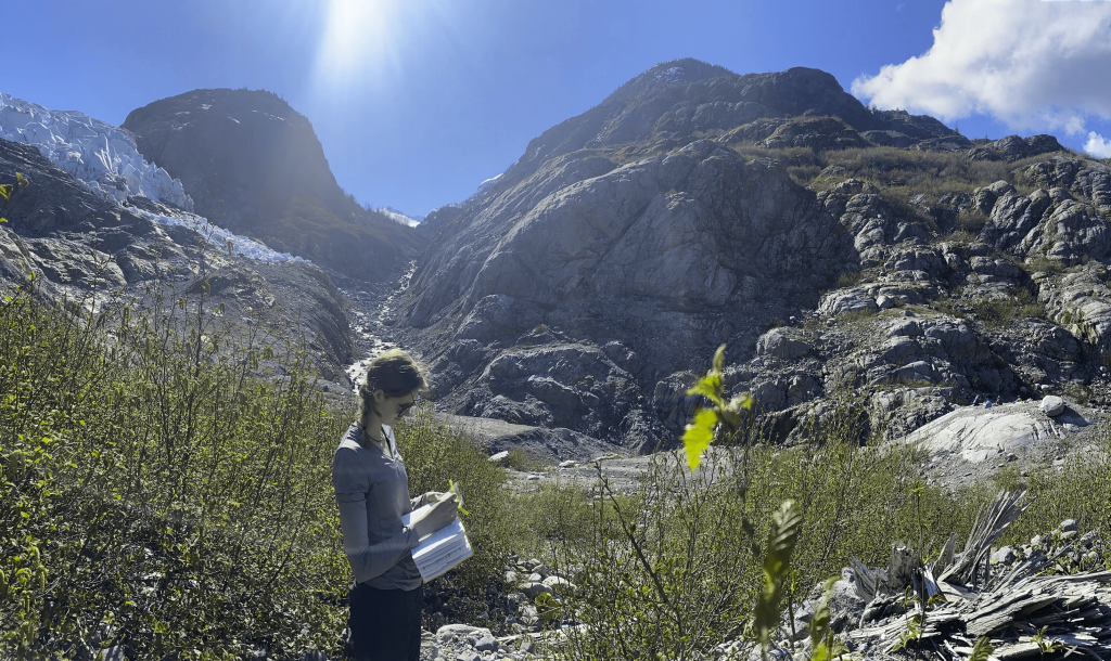 Student writing in a field in front of Herbert Glacier.