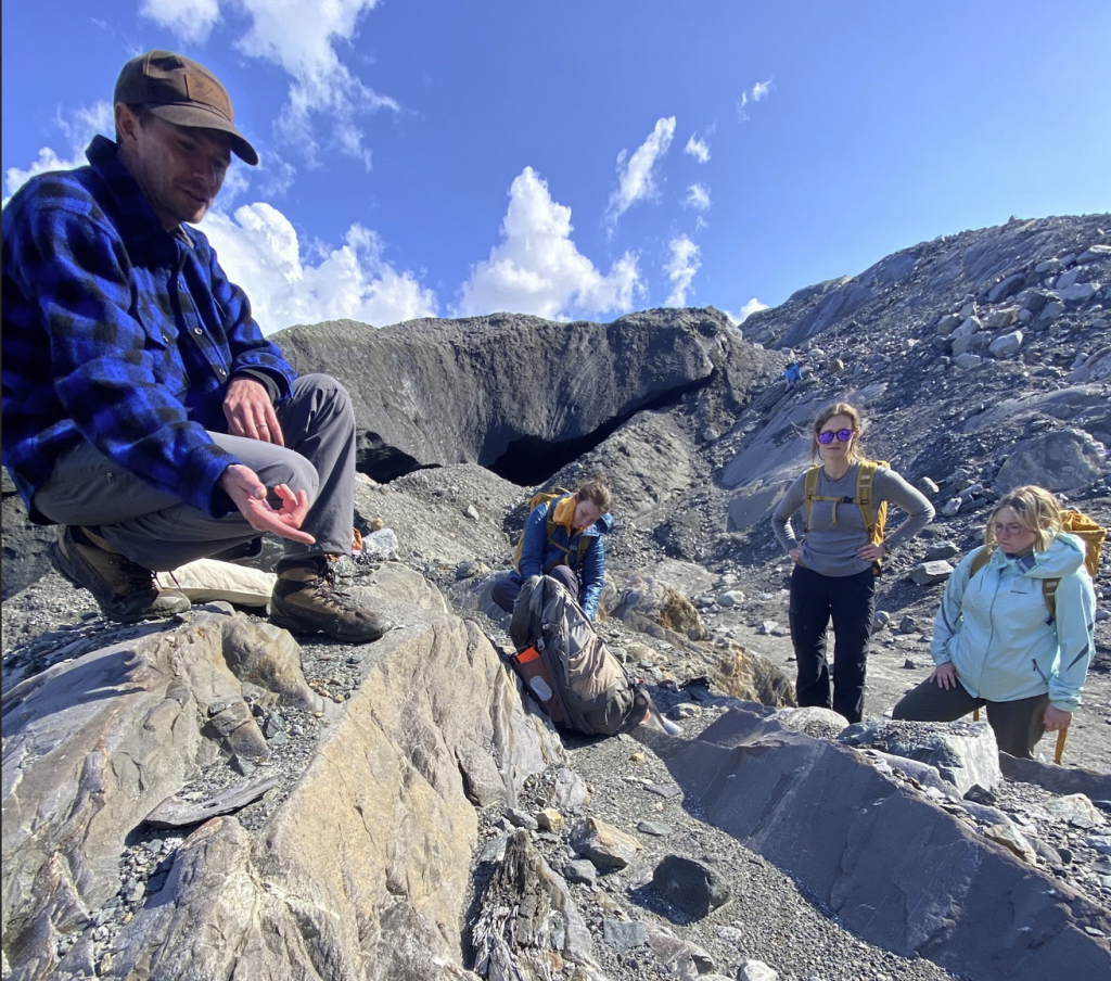 Professor showing rock outcrop to a group of students on a mountain.