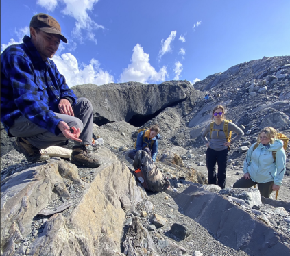 Professor showing rock outcrop to a group of students on a mountain.