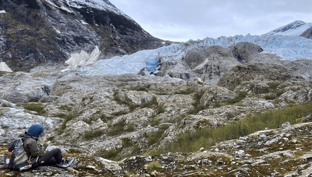 Student sitting and writing in front of Herbert Glacier.