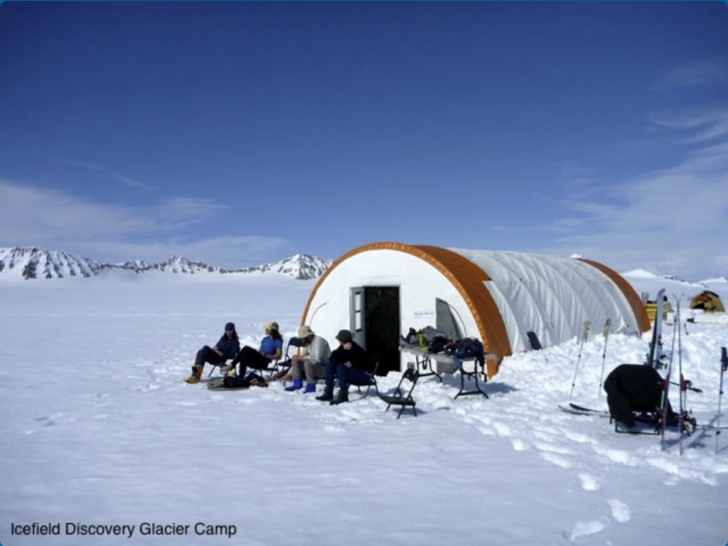 Group of people in snowfield sitting in front of shelter at Icefield Discovery Glacier Camp.