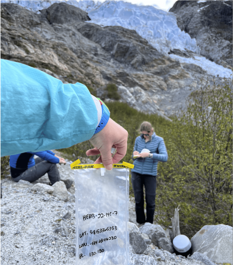 Student holding up sample bag in front of other students standing by a glacier.