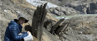 A student writing in a scientific journal, looking at the surrounding rocks and decaying wood.