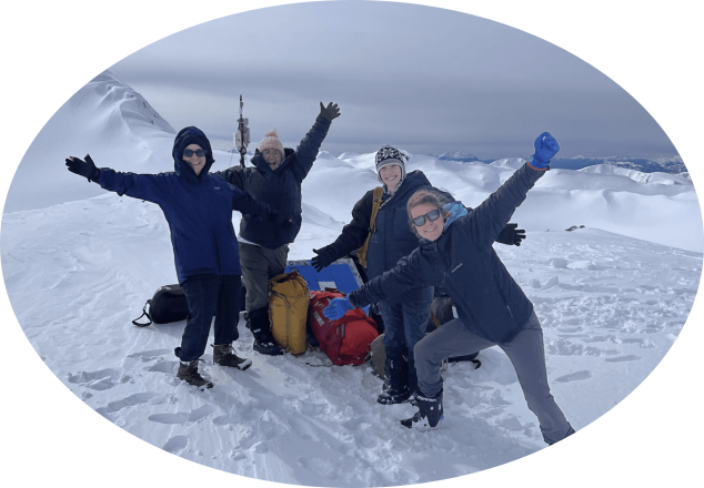 A group of students with scientific equipment posing on top of snow-covered mountains.