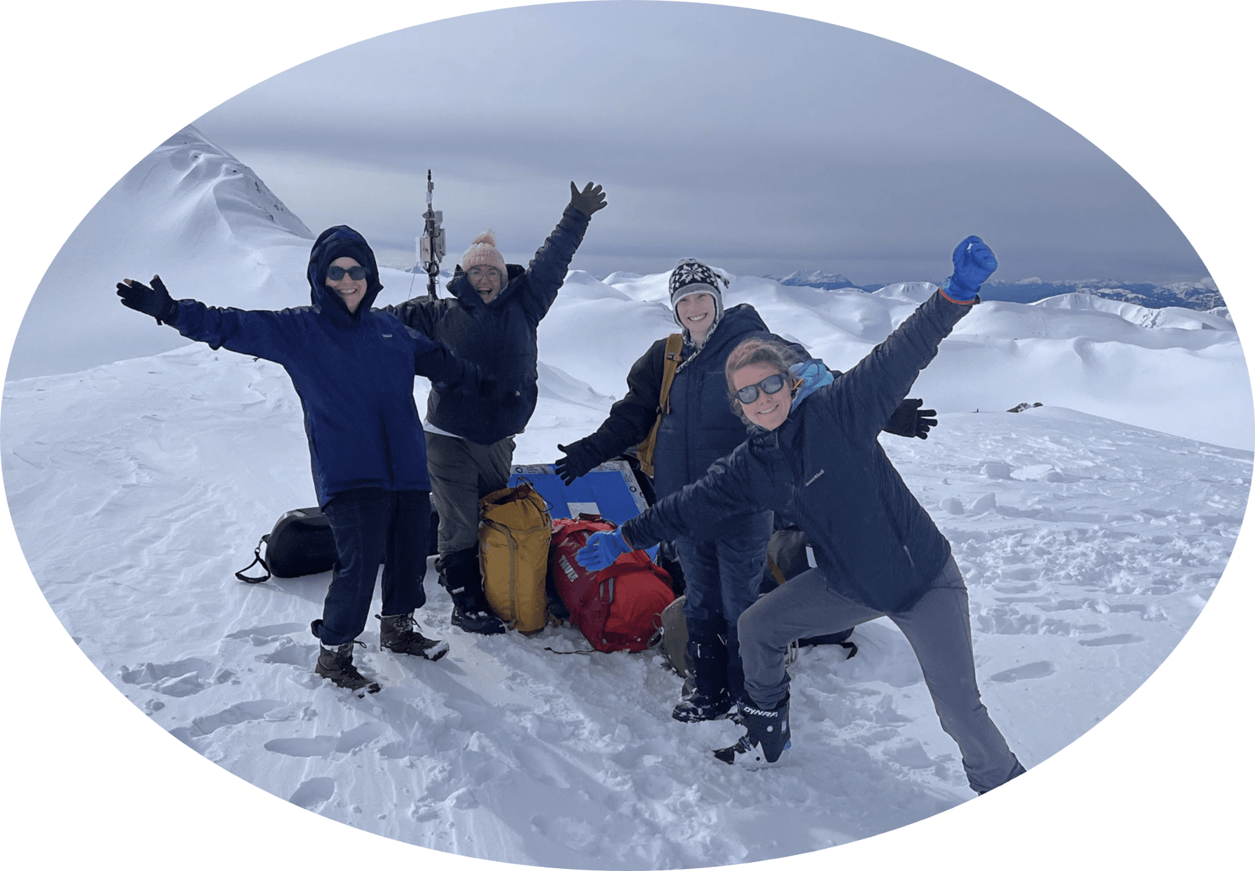 A group of students with scientific equipment posing on top of snow-covered mountains.