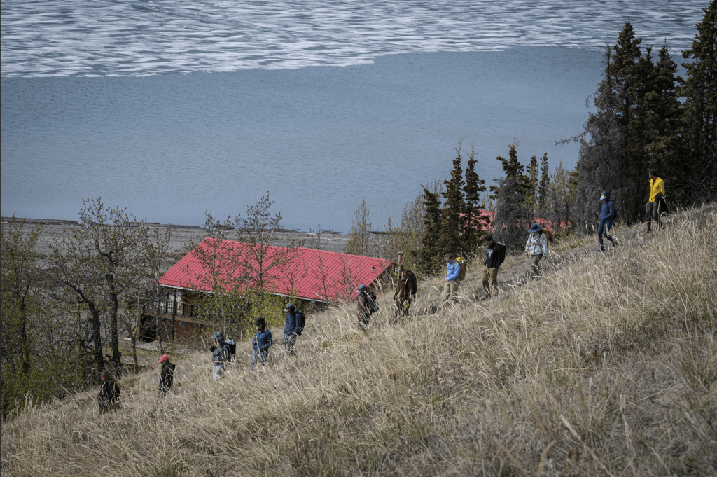 Students hiking down hill with camp and a lake in background