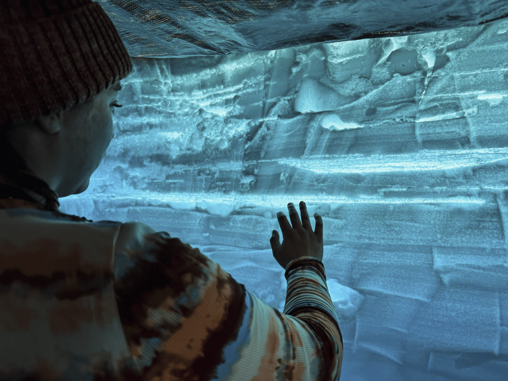 Student placing a hand on a backlit wall of blue ice