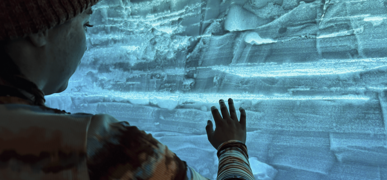 Student placing a hand on a backlit wall of blue ice