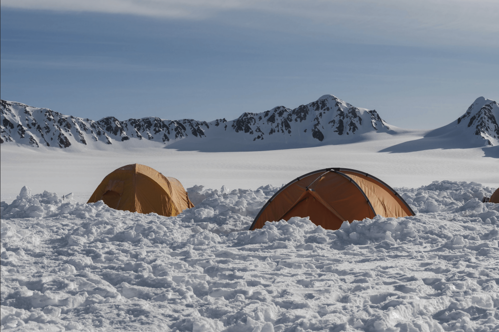 Two orange tents in a snowfield in the mountains