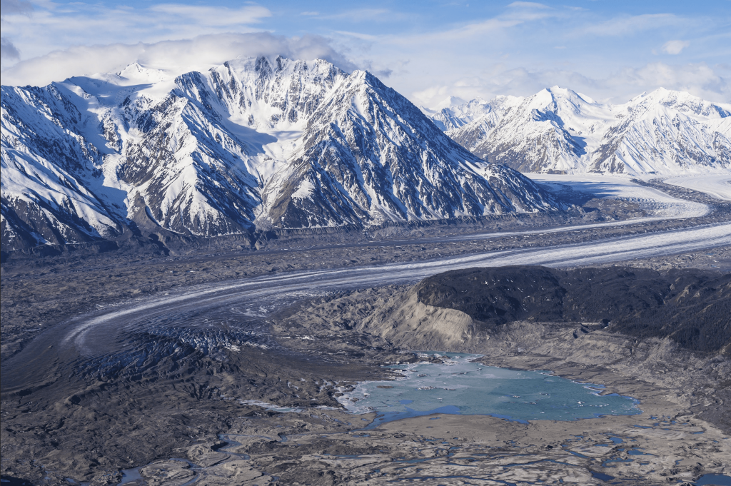 Landscape view of Kaskawulsh Glacier with dirt road and small lake in foreground