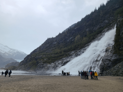 Group of students standing on a beach in front of a waterfall on a steep cliffside.