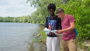 two smart students collaborate, looking at sampling instructions near the river