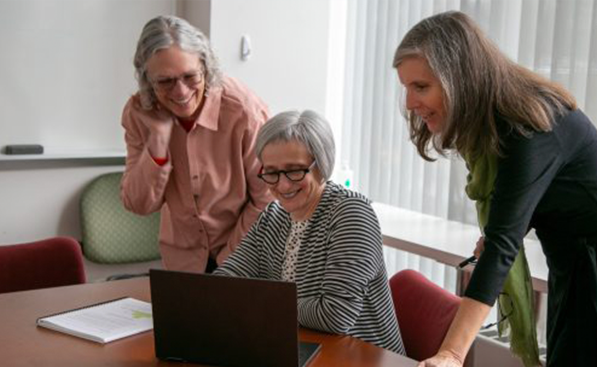 A photo of 3 women around a laptop