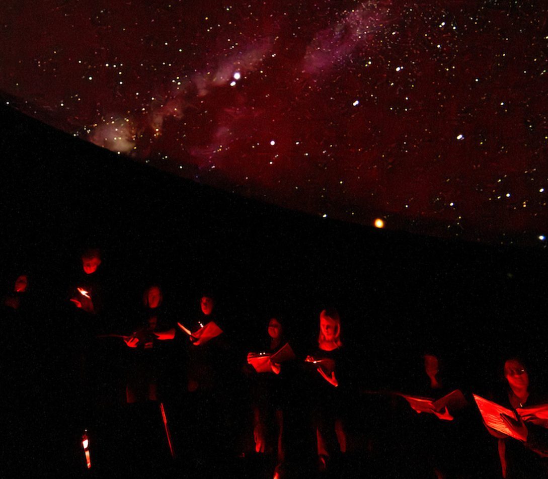 A photo of the Collegiate Choral singing in the planetarium 