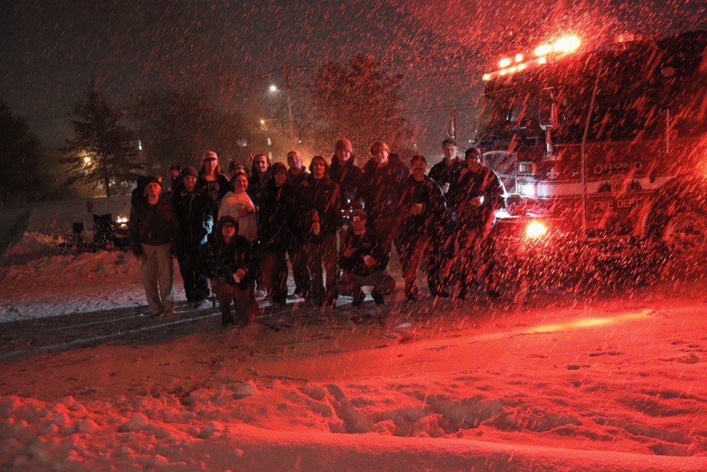Brothers of Sigma Chi stand outside with members of the Orono Fire Department while it snows