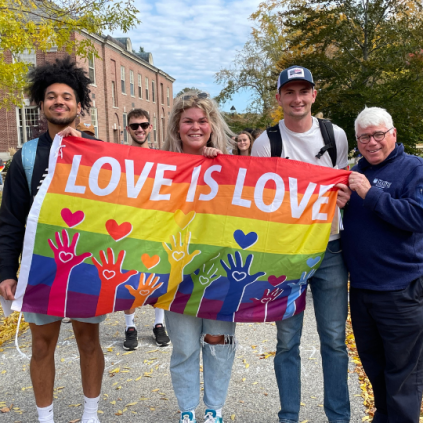 Students stand with Dr. Dana holding a flag that says love is love