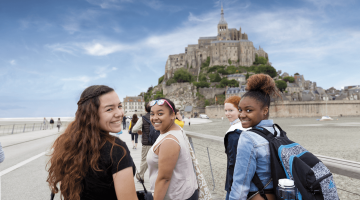 Three young women of color walking down a path to Mont Saint-Michel.