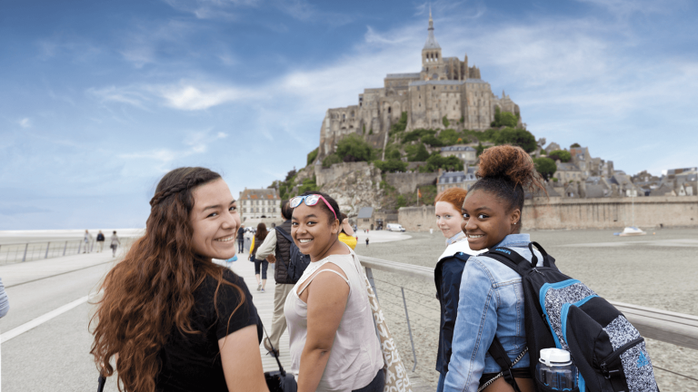 Three young women of color walking down a path to Mont Saint-Michel.