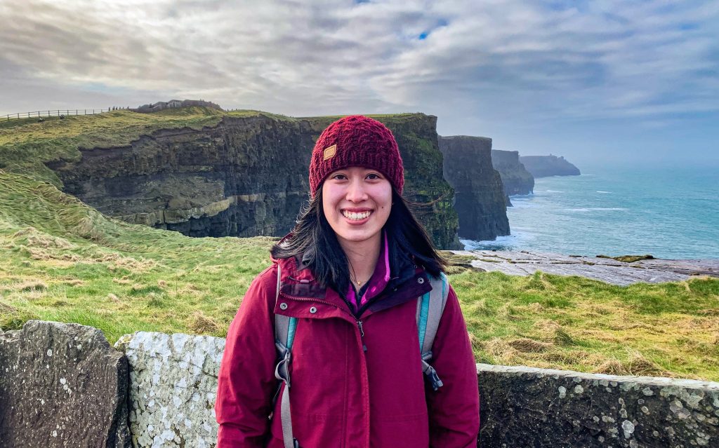 Asian female student standing in front of the Cliffs of Moher in Ireland.