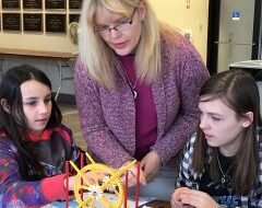 A female instructor helps two female students at an engineering summer camp in Orono Maine