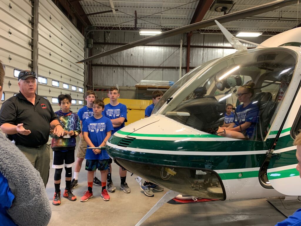 A group of young kids looking at a helicopter during the Maine Summer Transportation Institute summer camp in orono Maine