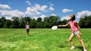 Young girls playing frisbee in an open field at RAD summer camp in Orono Maine