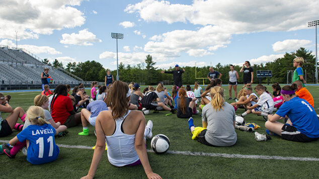students sitting on field at soccer camp