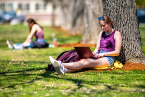 student on laptop outside next to tree