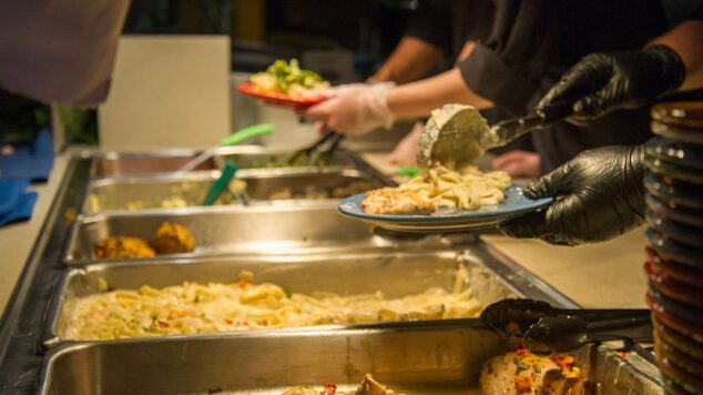 UMaine dining worker scooping pasta onto a plate.