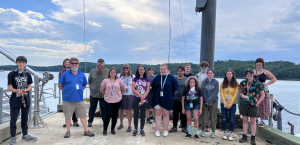 A group of students stand together on a dock, they are smiling for a group photo at the Darling Marine Center in Damariscotta, Maine.