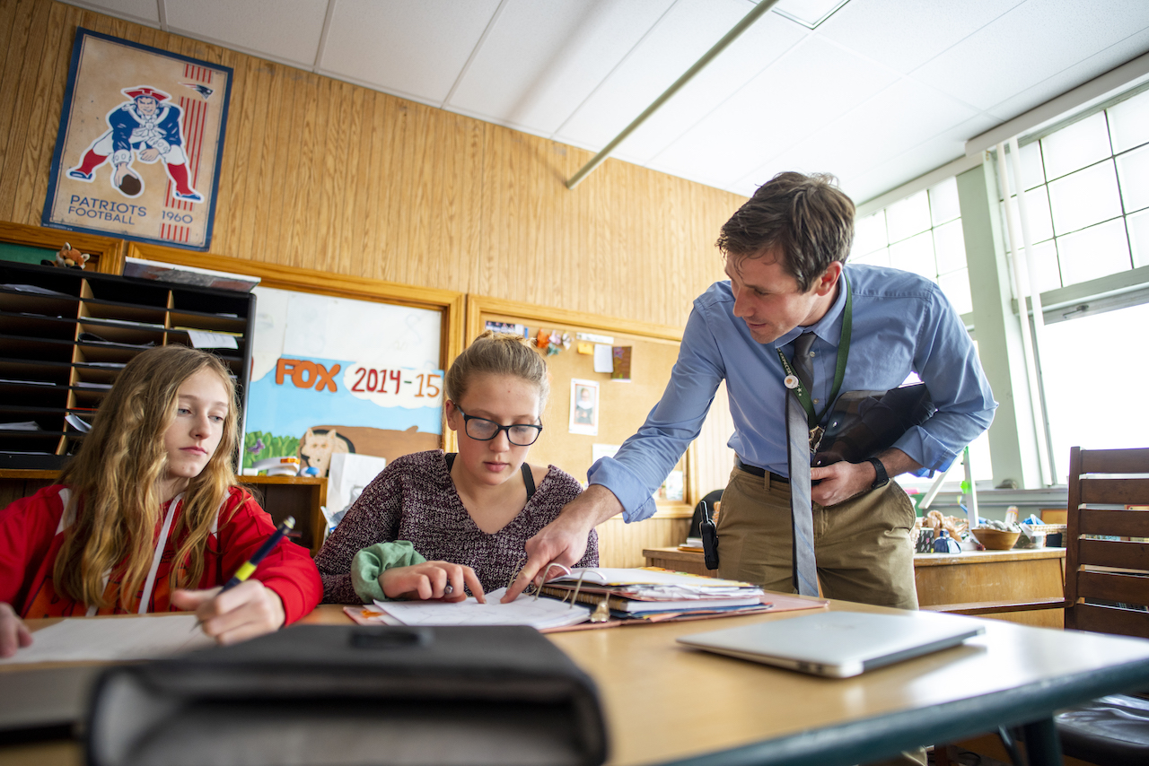 Teacher helping two high school students at their desk