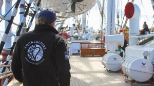 A photo of a person wearing a UMaine Aquaculture Research Institute jacket on the deck of a tallship