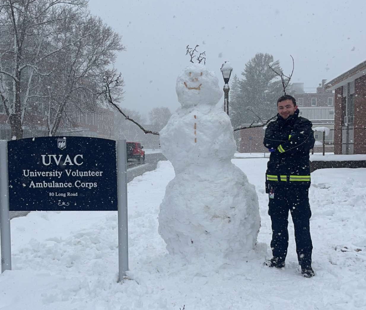 A UVAC member proudly stands beside a tall snowman next to the UVAC sign.
