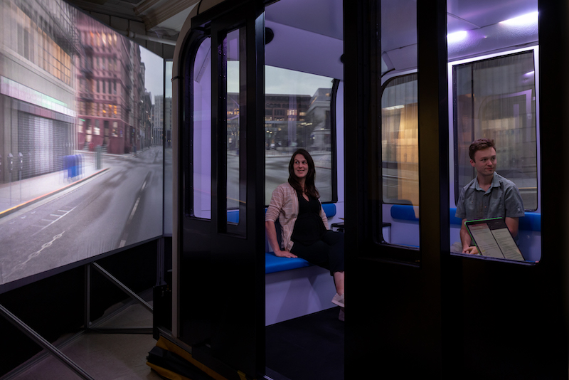 Two passengers are visible inside VEMI's autonomous vehicle simulator