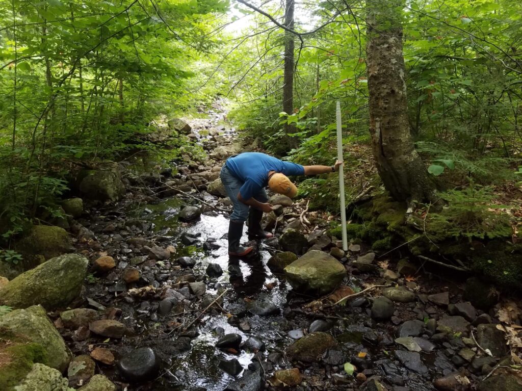 A researcher uses a stadia rod to measure bank height in a rocky headwater stream channel