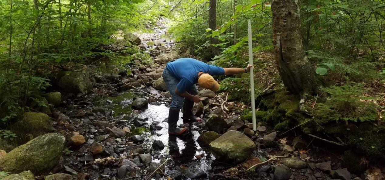 A researcher uses a stadia rod to measure bank height in a rocky headwater stream channel