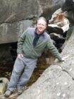 Associate Professor Sean Smith leaning on a large rock beside a stream