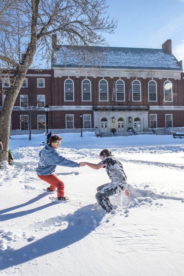 student getting up out of the snow in front of Fogler Libary