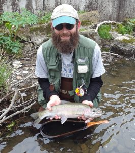 Steve on the bank of a stream holding a fish.