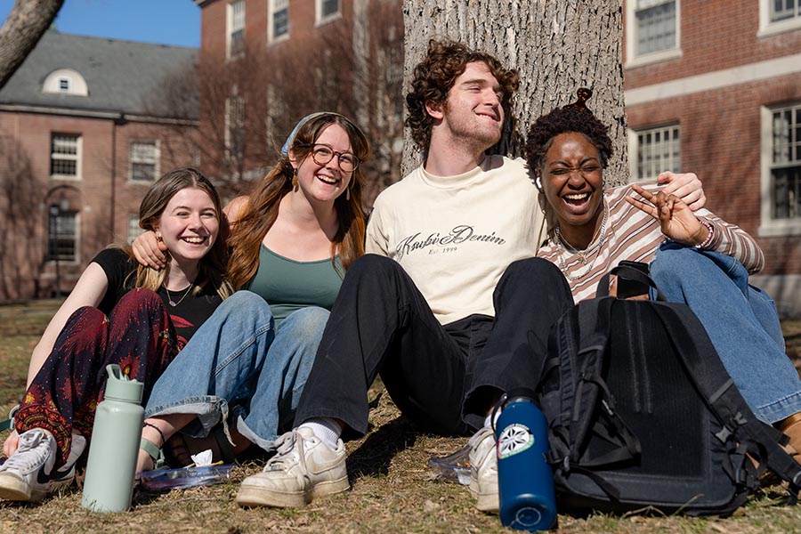 A photo of four people sitting in front of a tree, smiling for the camera