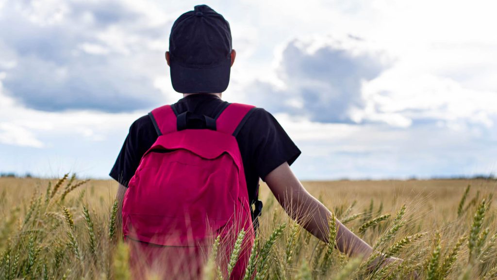 A photo of a person walking through a field wearing a red backpack