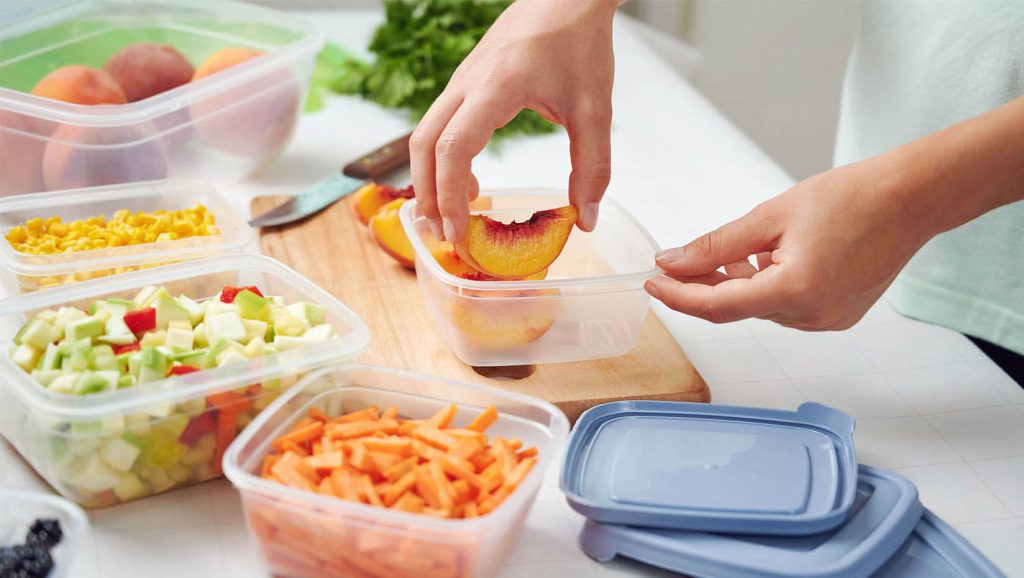 A photo of a person putting food into storage containers