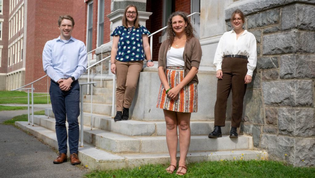 A photo of four humanities fellows standing in front of a brick building