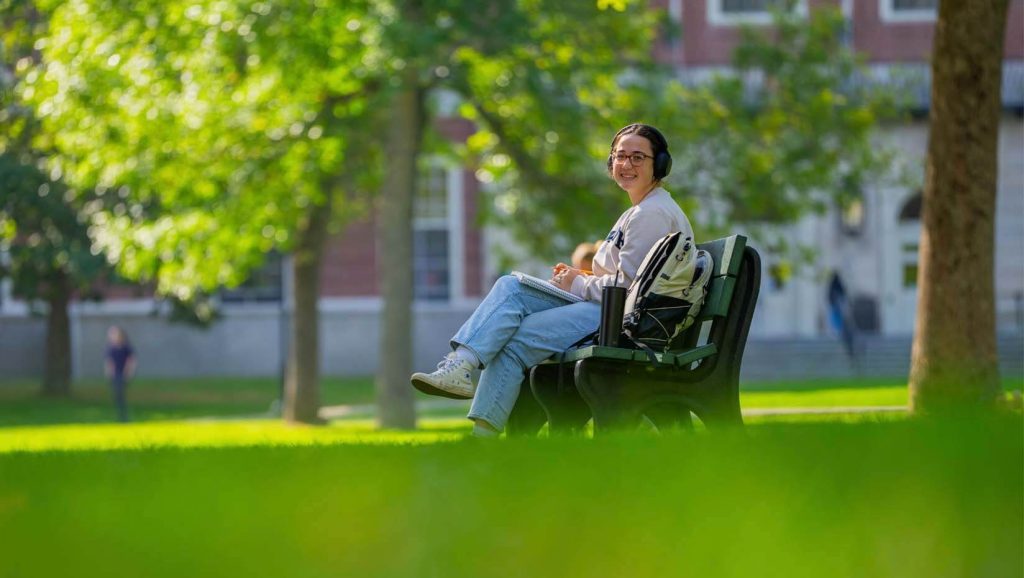 A photo of a person sitting on a bench on UMaine's Mall
