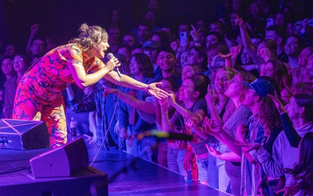 A photo of a person singing on stage and reaching out to the audience